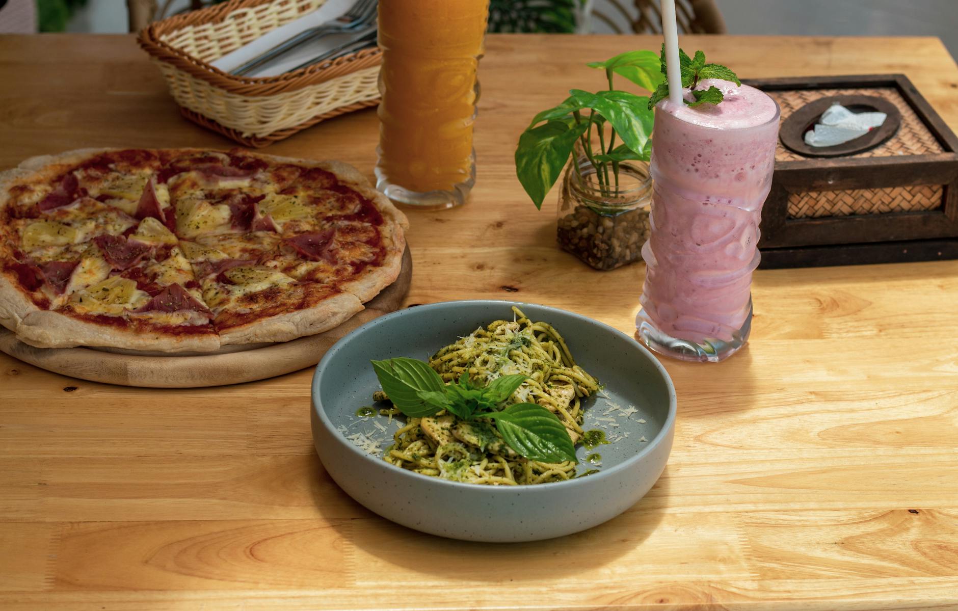 Pizza z pesto, makaronem i smoothie na drewnianym stole